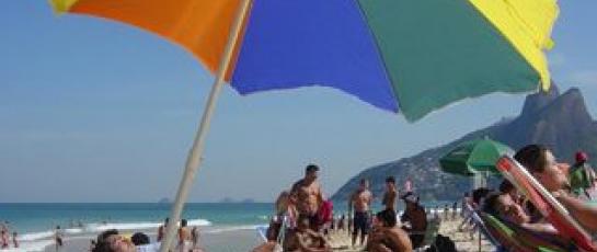 Sunbathers on a beach under a rainbow colored umbrella