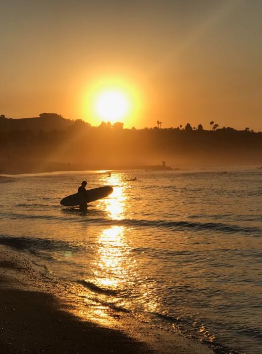 Sun setting behind the hill with silhouetted surfer entering the surf